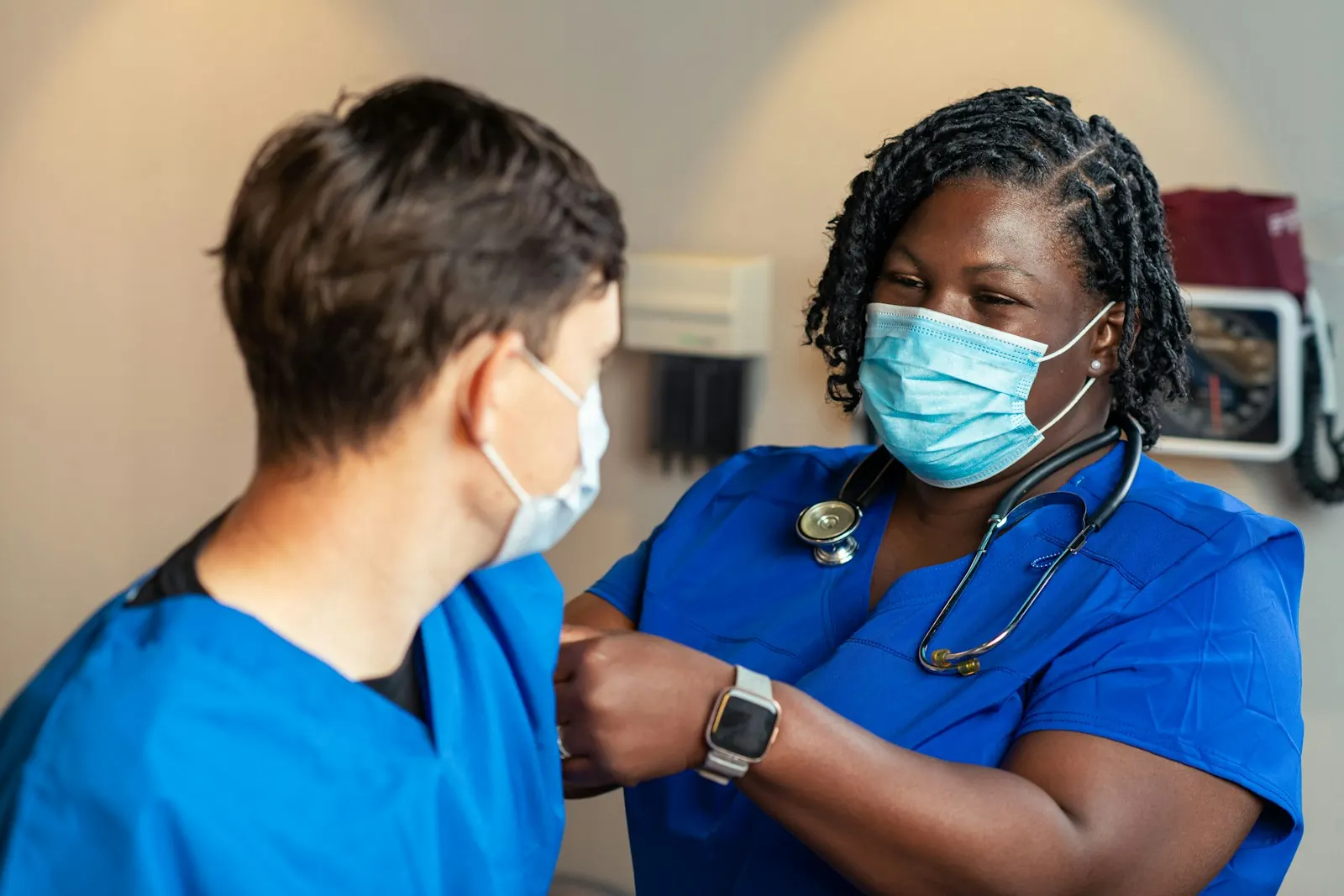 A nurse in blue scrubs talks with a colleague in a clinic.