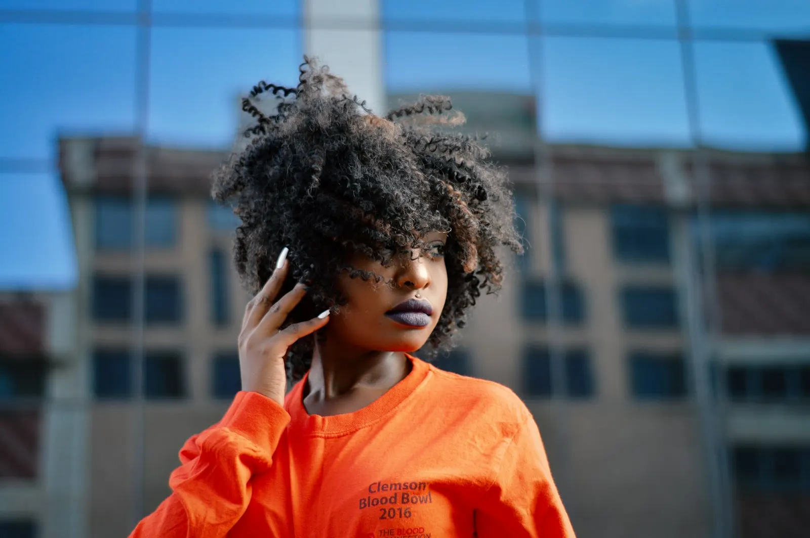 A woman in an orange top talks on her mobile phone outside.
