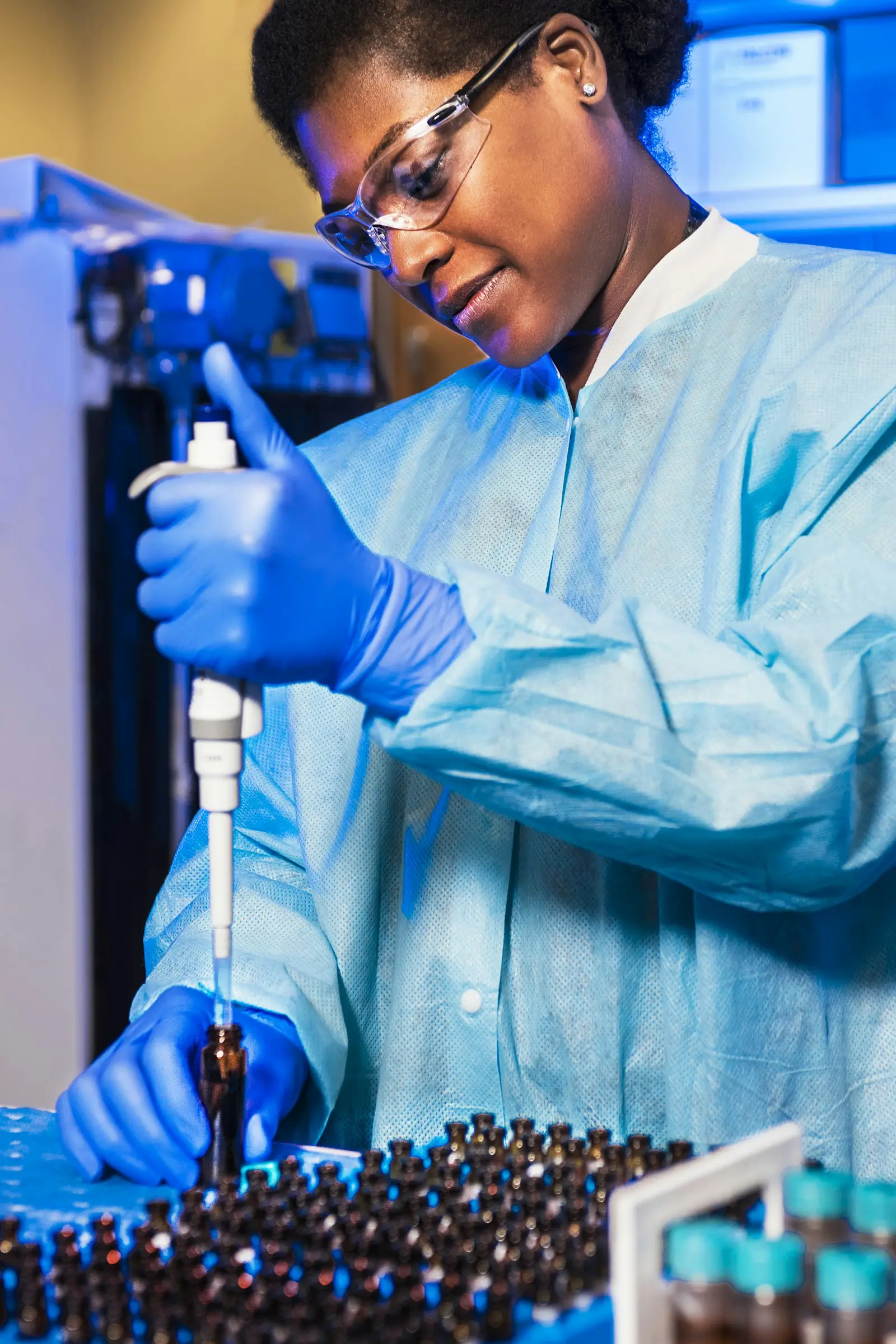 A laboratory scientist in protective glasses and gloves pipettes samples at the bench.